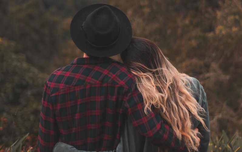 Man and woman with arms around each other facing nature background