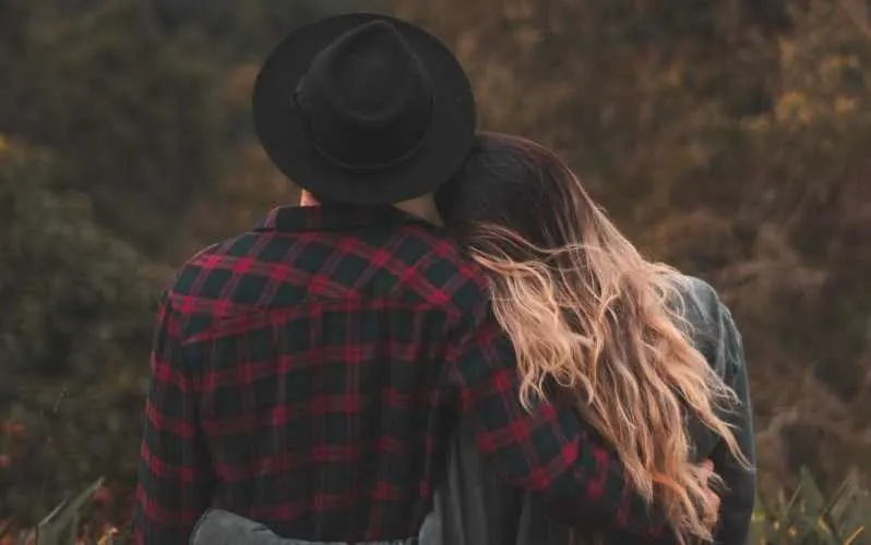 Man and woman with arms around each other facing nature background