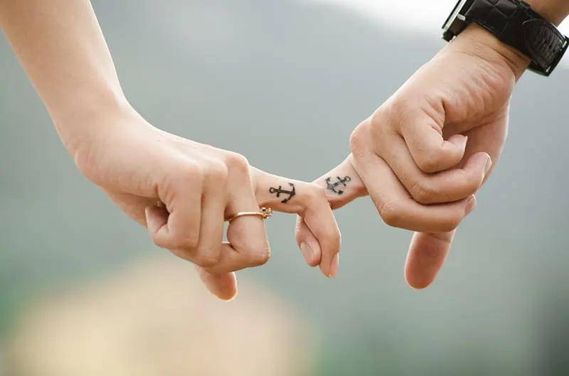 man and women interlocking index finger with anchor tattoos
