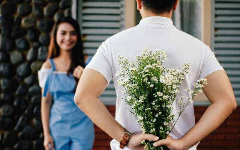 Uomo rivolto verso una donna felice con le mani sulla schiena e i fiori in mano