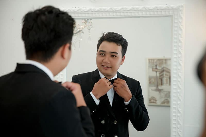 man holding his bow tie in front of a mirror