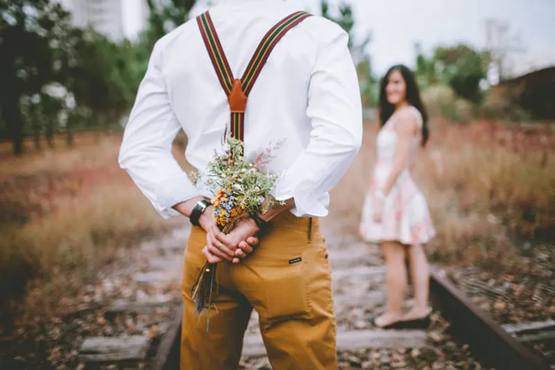 man holding the flowers behind his backs in front of the woman