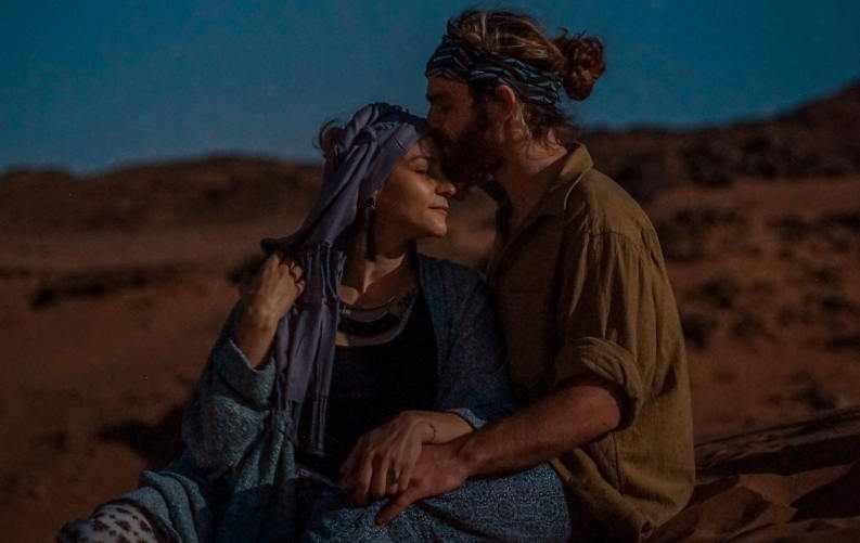 Homem a beijar uma mulher na testa, num fundo de deserto, à noite