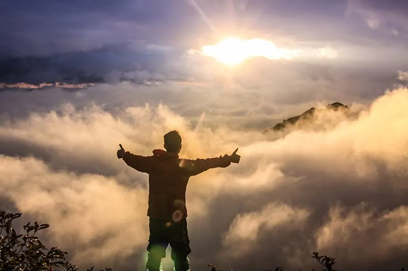 Man at mountain top during sunset arms spread out thumbs up