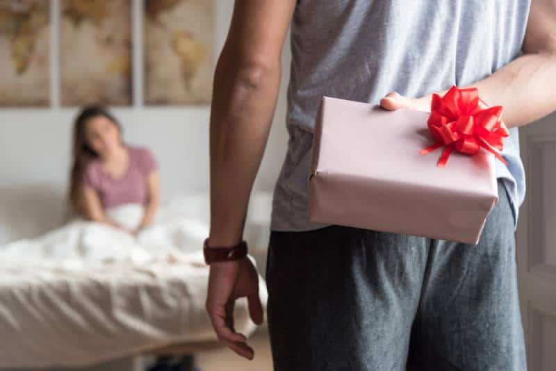 man suprise his girlfriend with present in bed