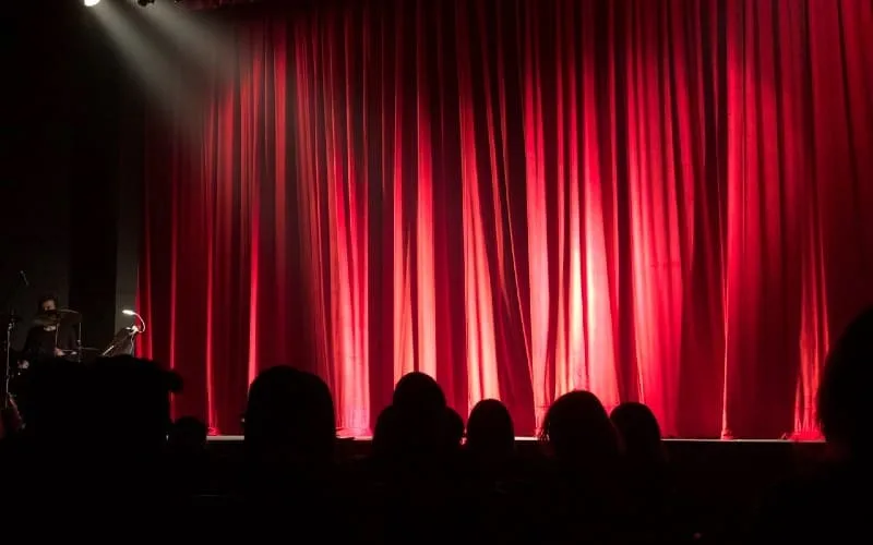 People at theater in front of red stage curtain