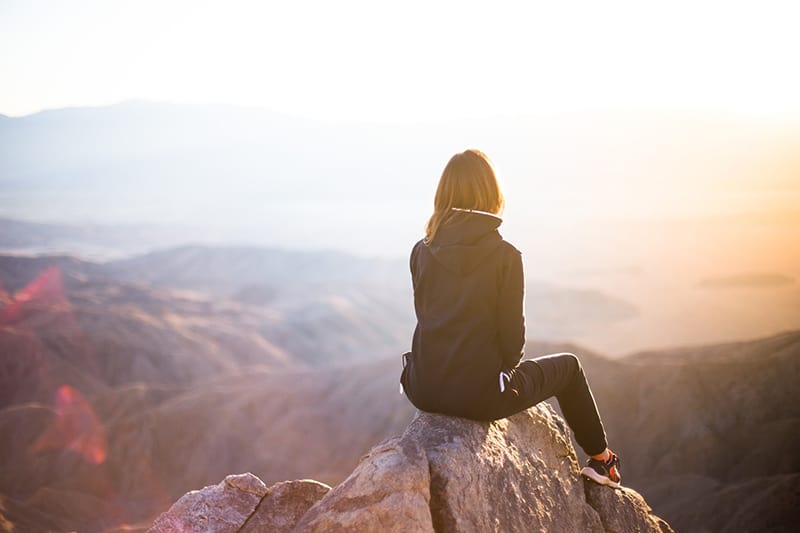 person sitting on top of the rock overlooking mountain 