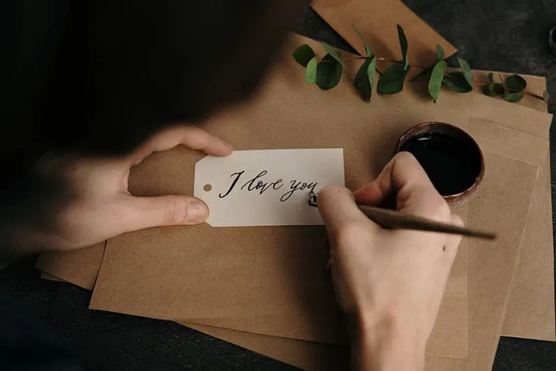 person writing note i love you with brown paper beneath