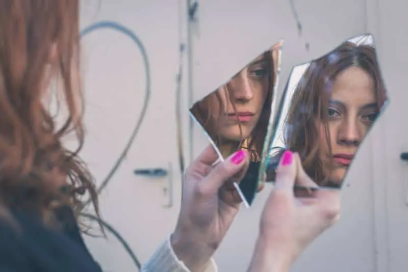 readhead woman looking herself in broken mirror