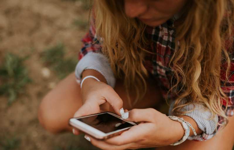 Jovem triste com cabelo comprido a enviar mensagens de texto para o telemóvel numa paisagem natural