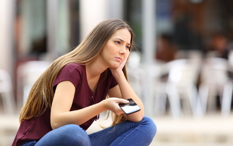 Camisa triste sentada con el teléfono en una mano al aire libre durante el día