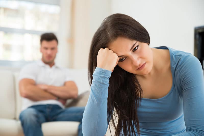 sad woman looking away while man sitting on the couch