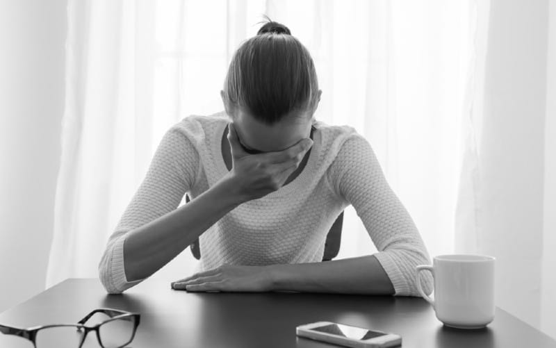 mulher triste sentada com a mão na palma da mão em frente a uma mesa com um smarthone