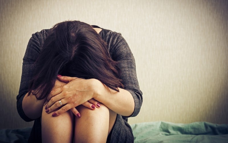 Sad woman with head on knees sitting against wall