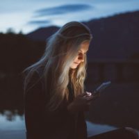 Mujer triste enviando un mensaje de texto por la noche junto al lago