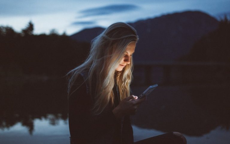 Mulher triste a enviar uma mensagem de texto ao anoitecer junto ao lago