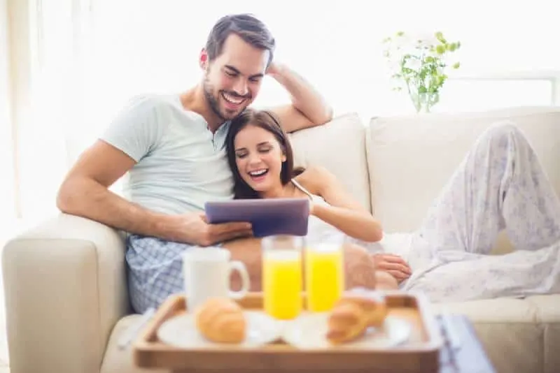 smiling couple at bed typing tablet