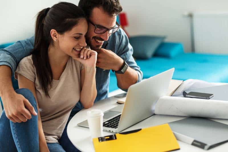 smiling couple sitting at home and looking at laptop screen