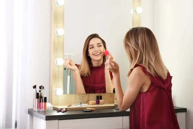 smiling woman applying makeup in front of mirror