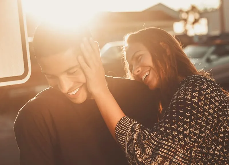 smiling woman holding hand on mans face during sunset