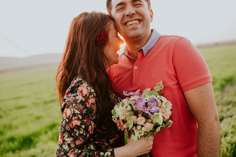 smiling woman hugging smiling man while holding flowers