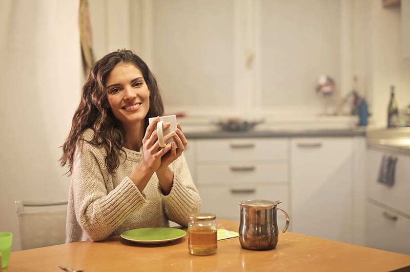 smiling woman in beige knit sweater holding white mug