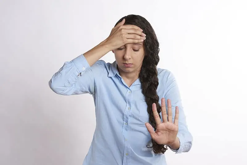 stressed woman in white top holding head