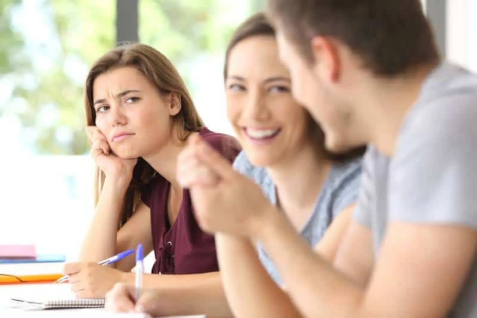 the man and woman laugh while the other woman looks at them angrily