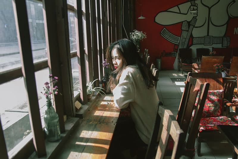 mulher pensativa sentada junto às janelas de um café