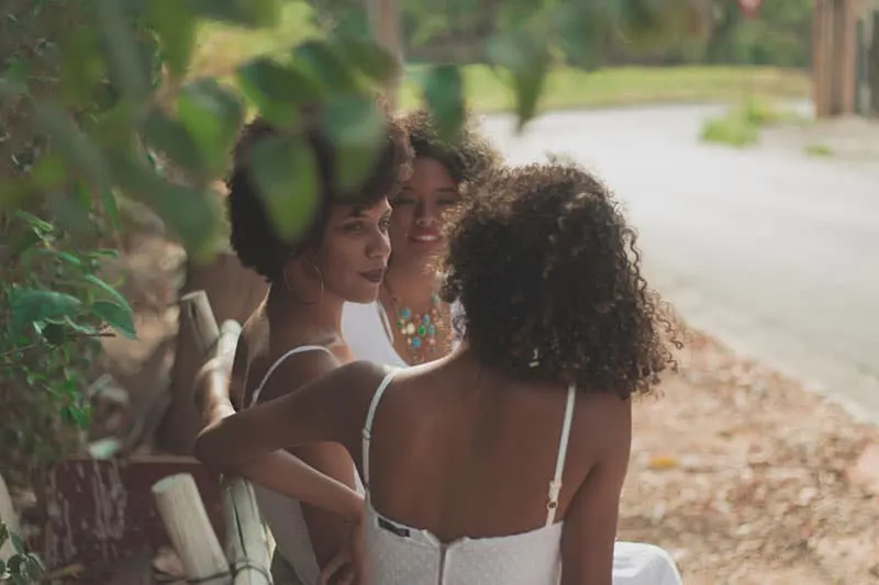 three women sitting in a bench under a tree
