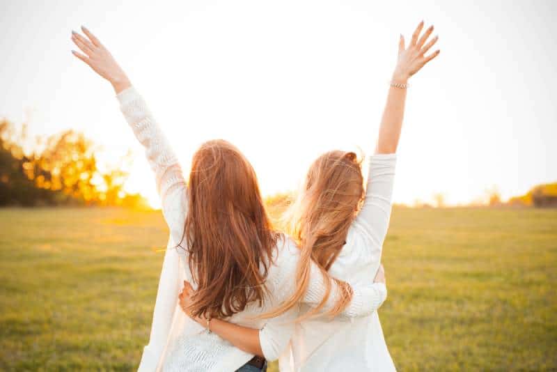 two girl hug with hands up in nature