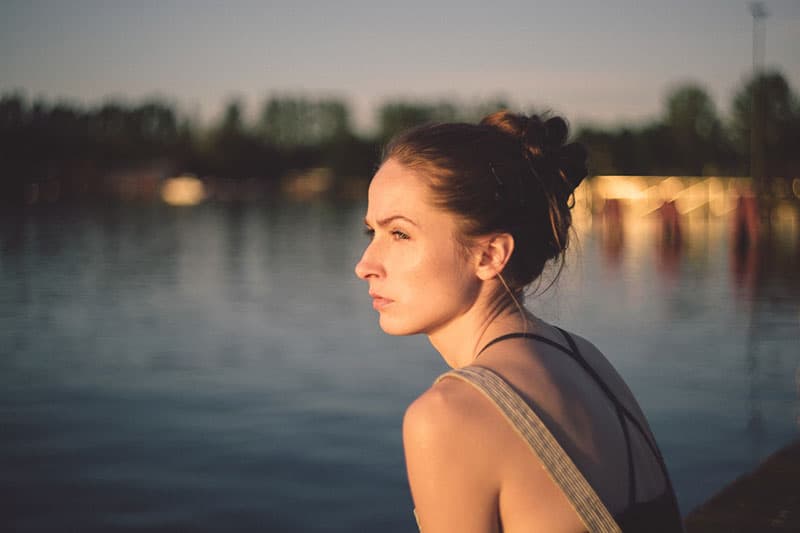 mulher junto ao lago com uma cidade desfocada no fundo