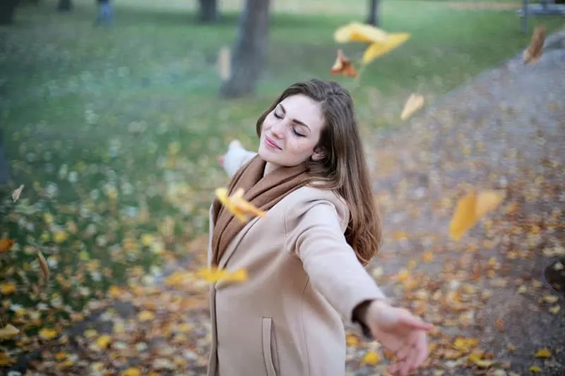 woman in coat feeling the moment with falling leaves