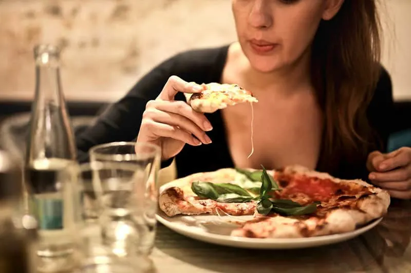 woman holds sliced pizza by the table with glass
