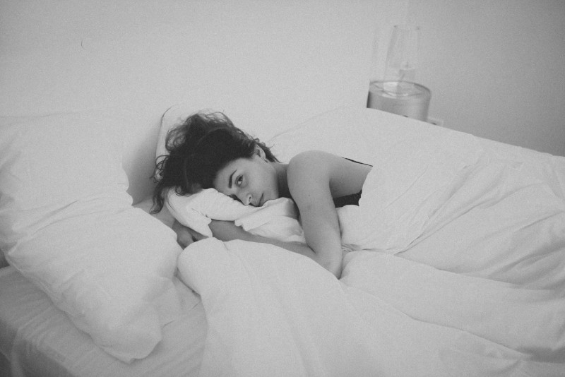donna sdraiata sul letto coperta da una coperta bianca