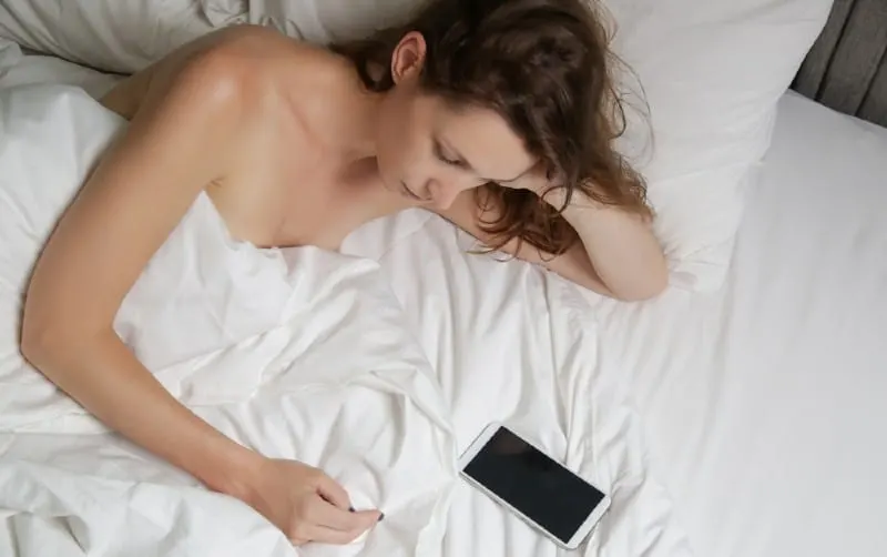 Sad woman laying in bed and looking at phone
