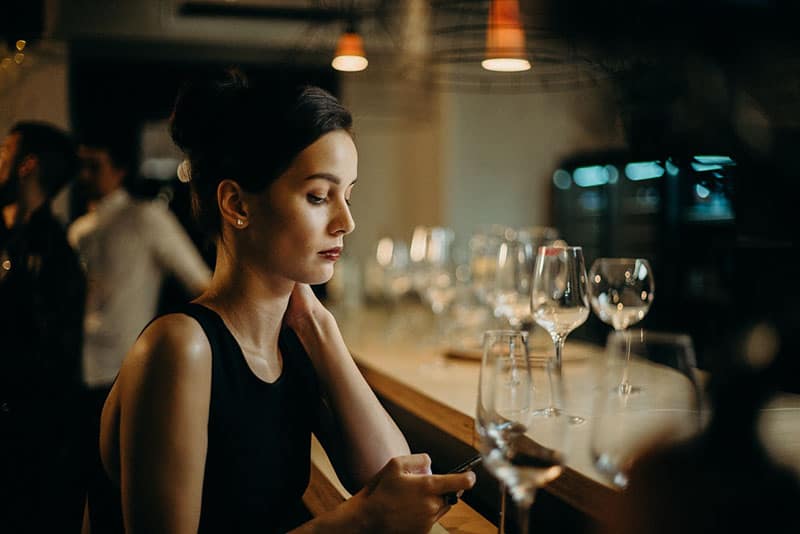 woman in black dress leaning on table texting