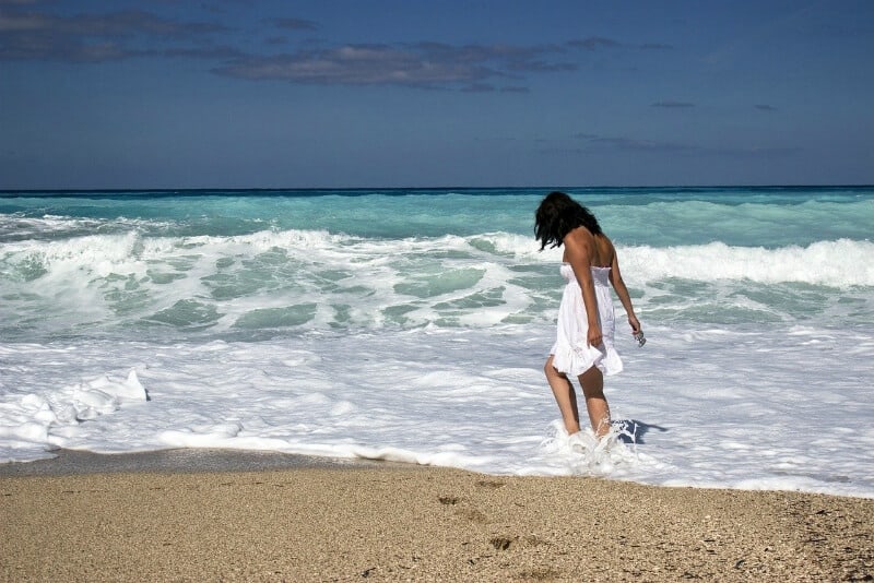 Mujer con vestido blanco caminando entre olas 