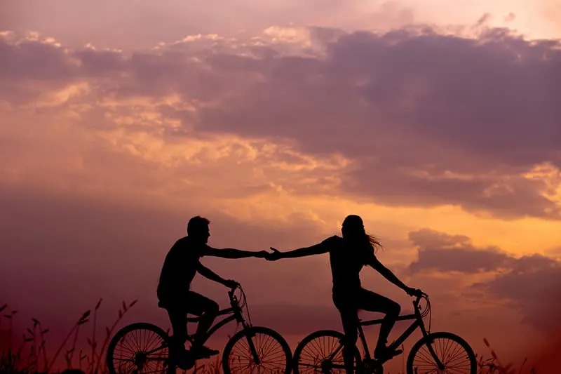 a woman on a bicycle reaches for a mans hand behinde her also on bicycle