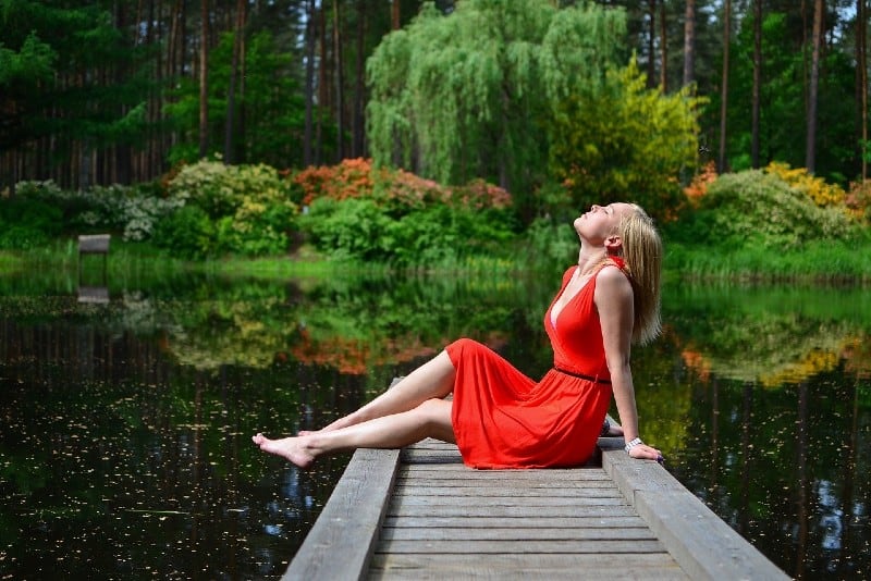 blonde woman in red dress sitting on dock by lake