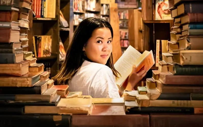 Woman in white top reading in a bookstore surrounded by books