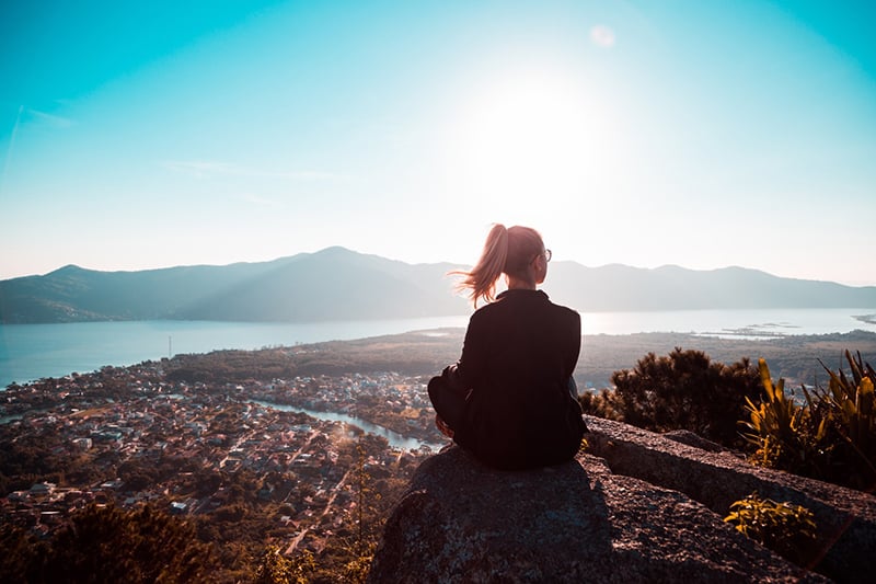 woman sitting at the edge of the mountain watching city