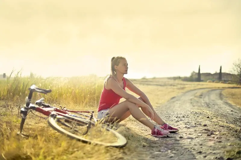 woman -sitting-by-the-side-of-a-dirt and a bike
