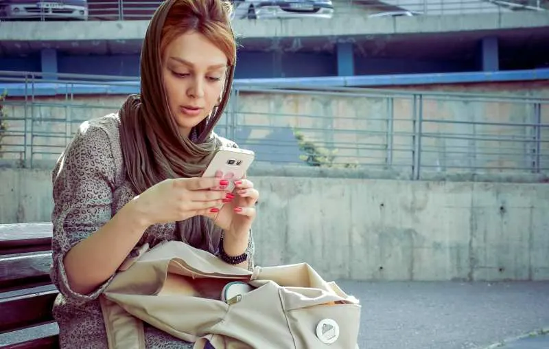 Woman with scarf on her head sitting on a bench and texting on her phone