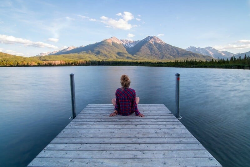 Mujer rubia sentada en el muelle junto a un lago