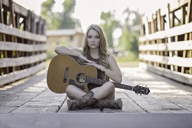 woman-sitting-while-holding-classical-guitar sitting on a wooden bridge 