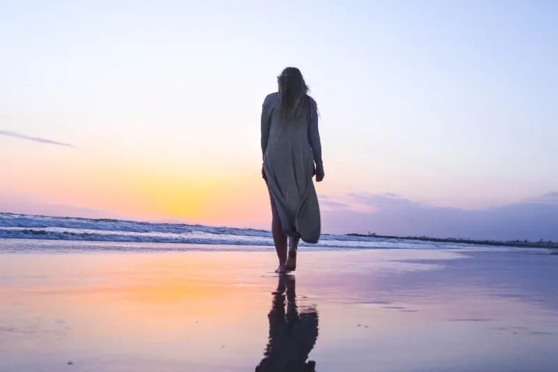 woman in long cardigan walking on beach during sunset