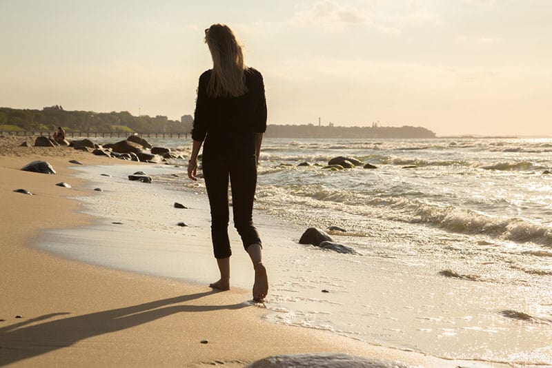 mulher a caminhar na areia junto ao mar