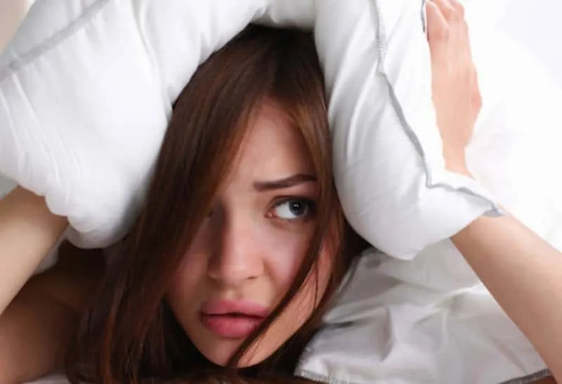 worried woman holding her head with pillow