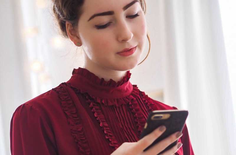 Mulher jovem de vestido vermelho a enviar mensagens de texto para o telemóvel